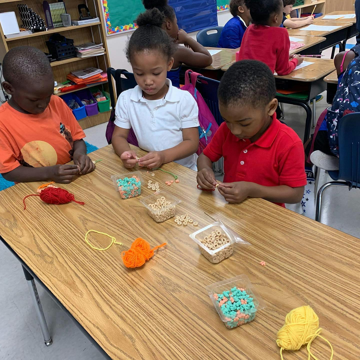 Three children at a table making crafts with yarn and beads
