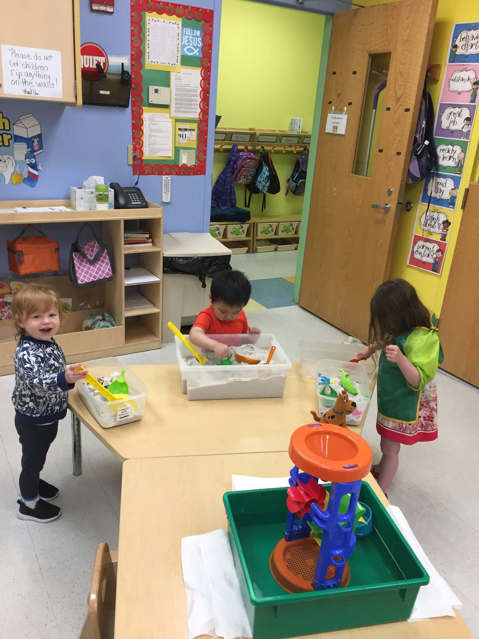 Three children playing with sensory bins in a classroom