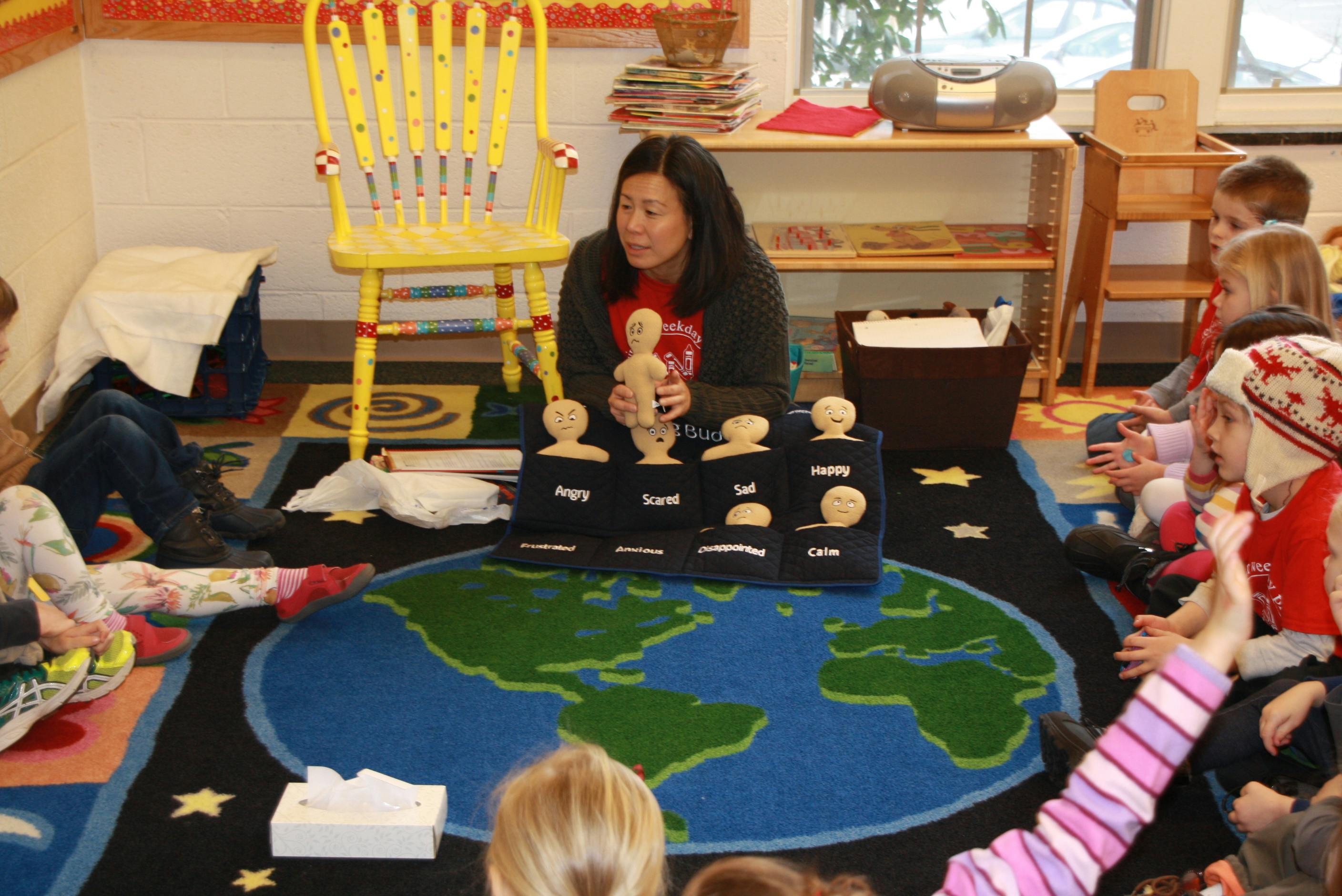 Person teaching children in a classroom with a world map rug