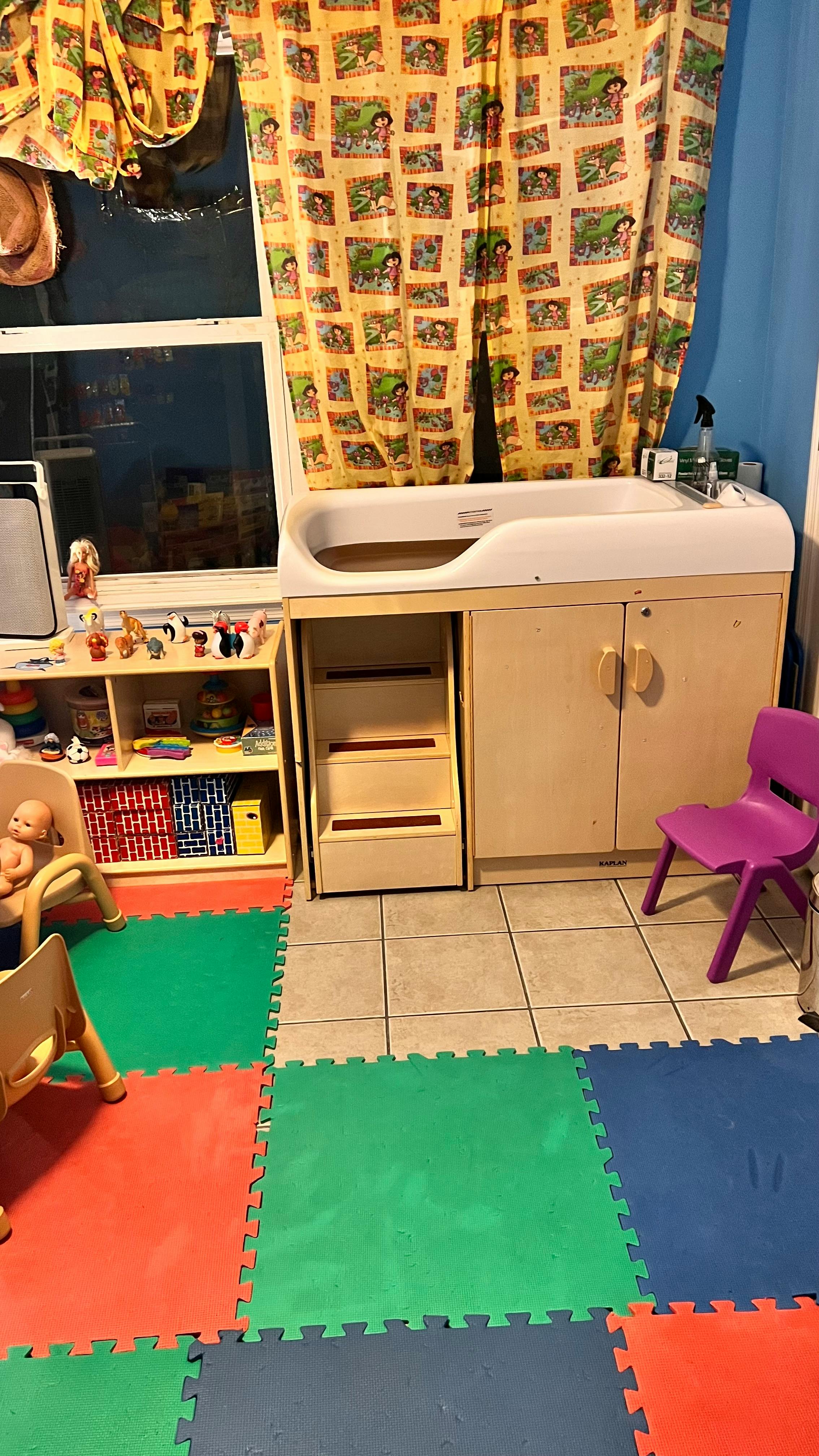 Changing station with a sink, steps, and storage cabinets in a room with colorful floor mats