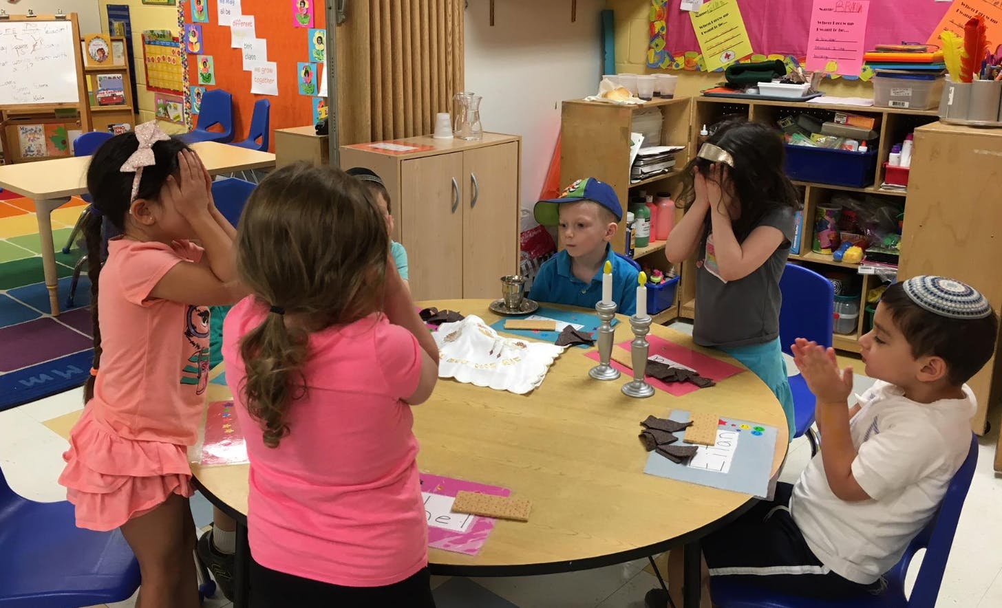 Children covering their eyes at a table in a classroom