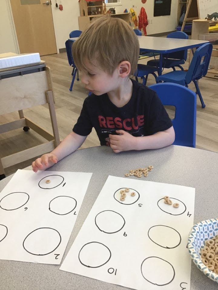 Child counting cereal pieces into drawn circles on paper