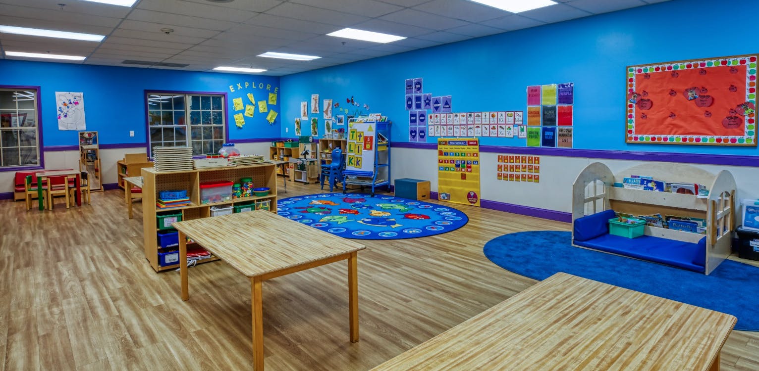Classroom with tables, chairs, shelving units, and learning materials on the walls