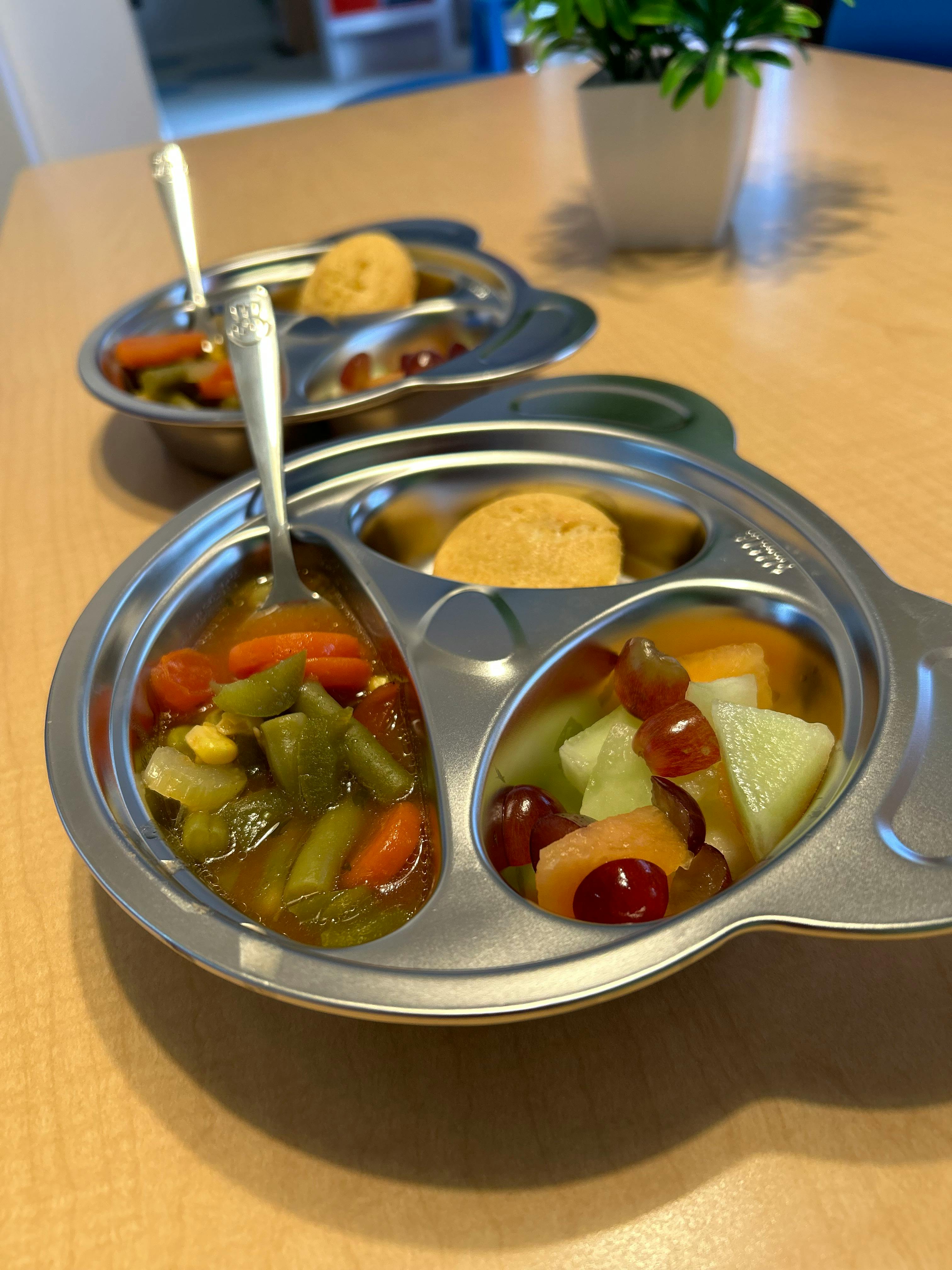 Two metal divided plates with vegetables, fruit, and a muffin