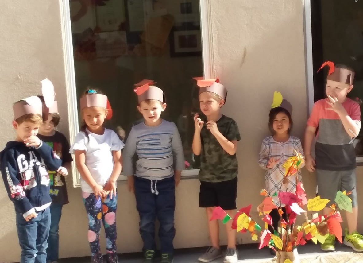 Six children wearing paper hats standing in front of a window