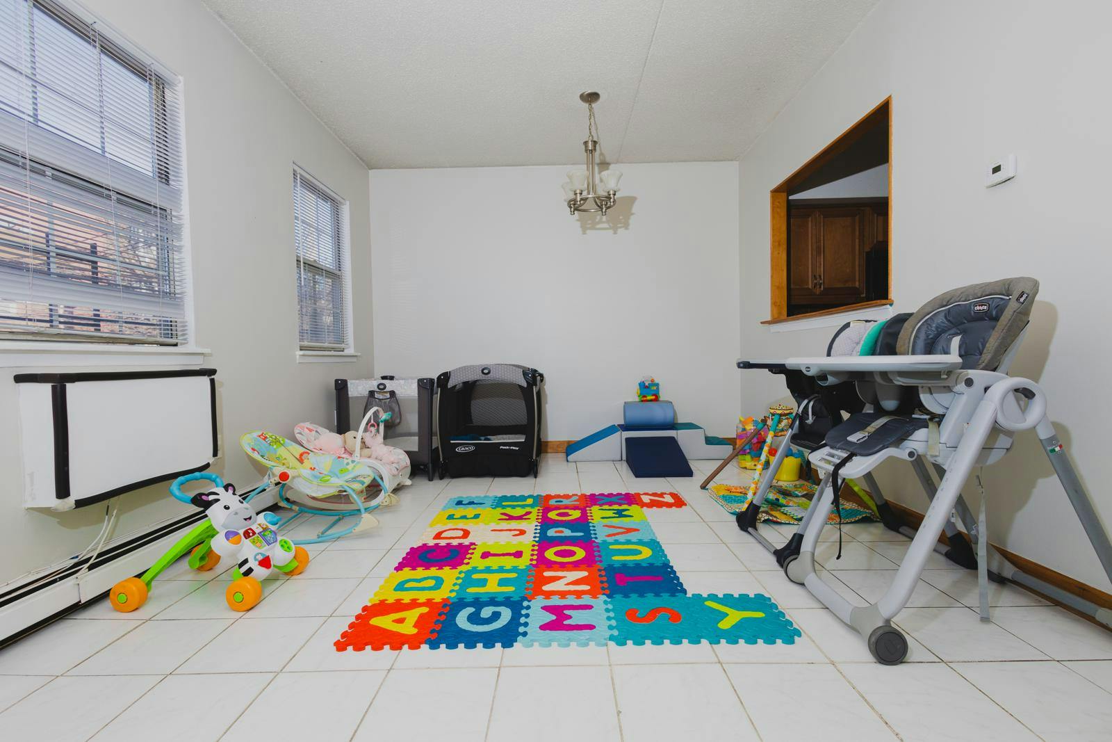 Room with alphabet play mat, high chair, and baby rocker