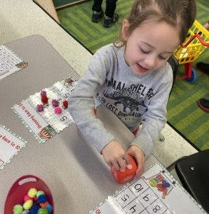 Child playing with a red toy and number cards at a table