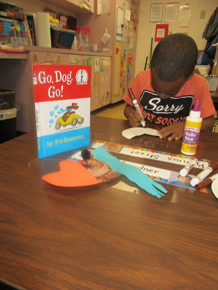 Child drawing at a table with a book titled "Go, Dog. Go!"