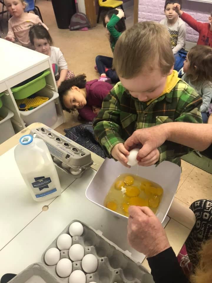 Child cracking an egg into a bowl with help from an adult