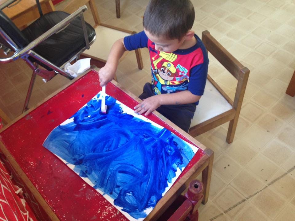 Child painting with blue paint on paper at a table