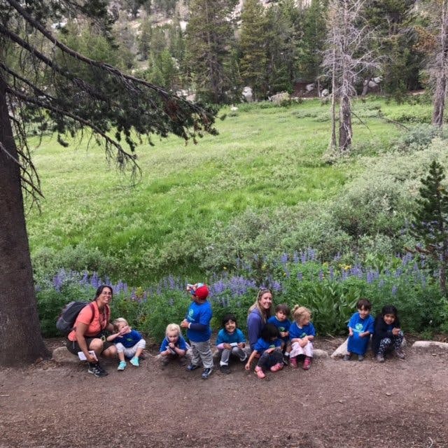 Two adults and several children sitting on a dirt path in a field