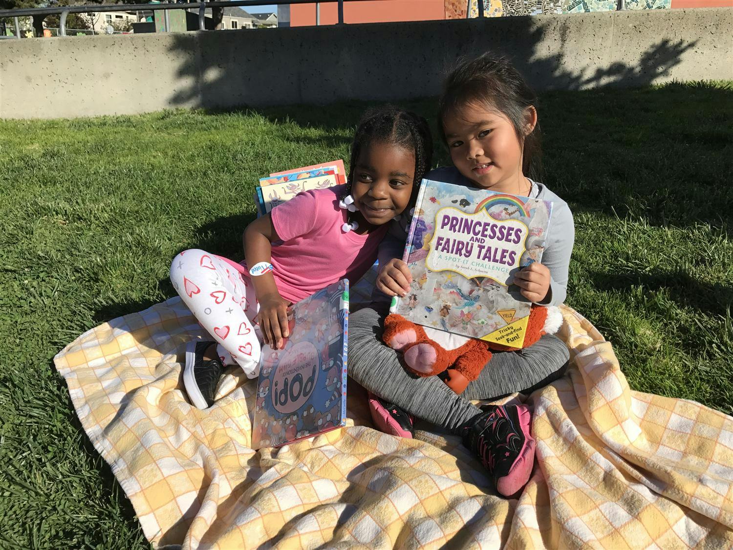 Two children sitting on a blanket with books, one holding "Princesses Fairy Tales"