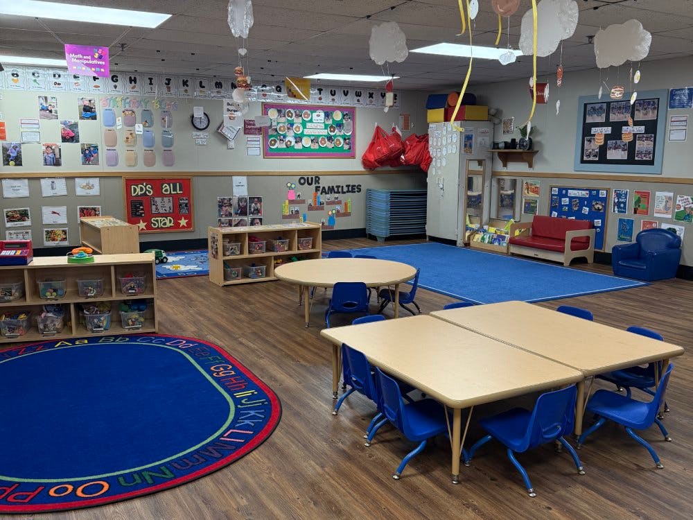 Classroom with small tables and chairs, shelves with toys, and wall decorations