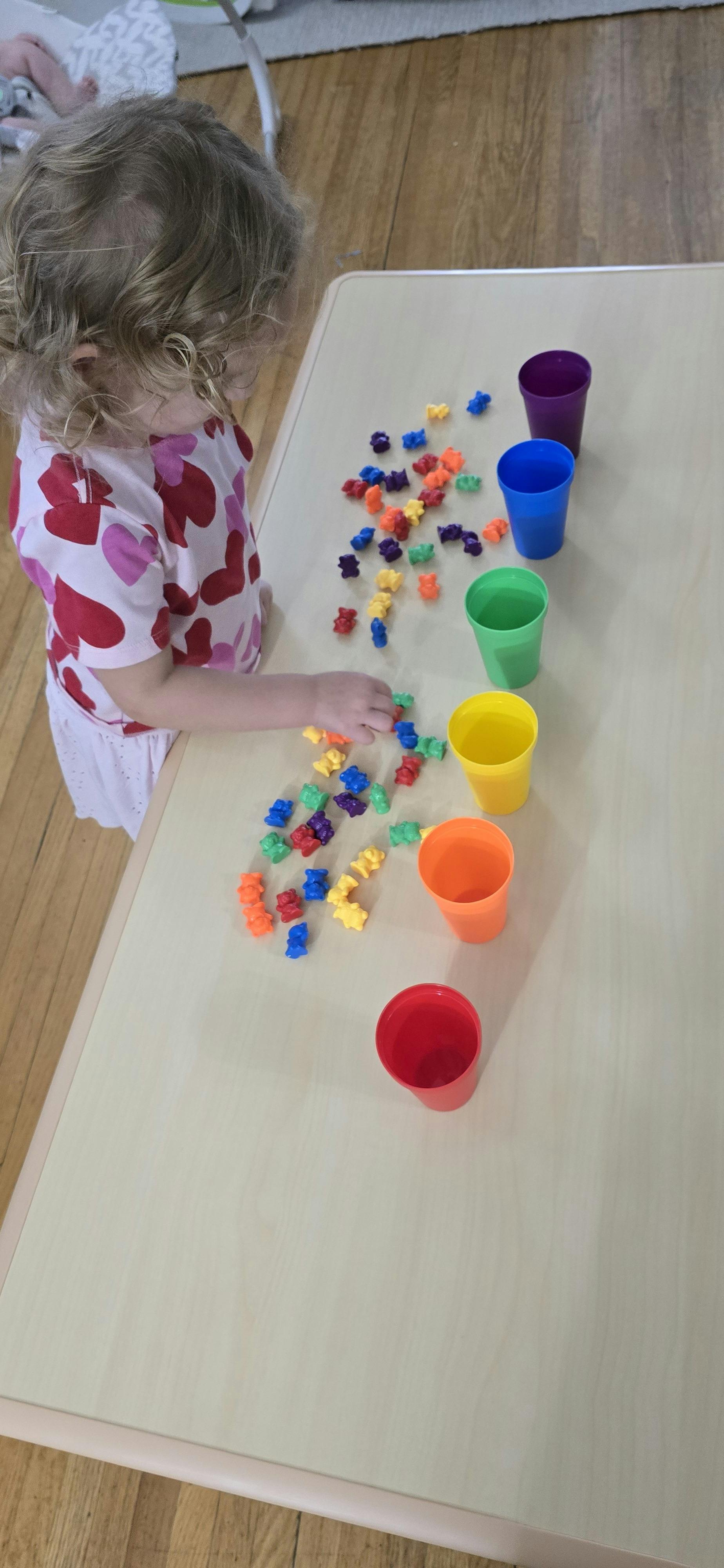 Child sorting small colorful bear figurines into matching plastic cups on a table