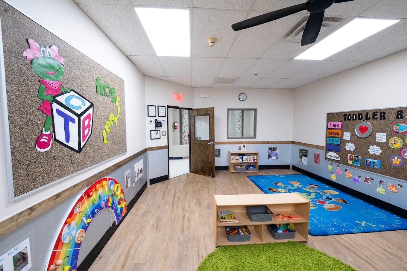 Empty toddler classroom with a blue activity rug, wall art, and toy storage