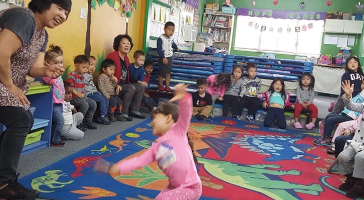 Adults and children in a classroom, one child dancing