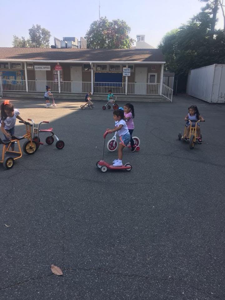 Children playing with scooters and tricycles on pavement