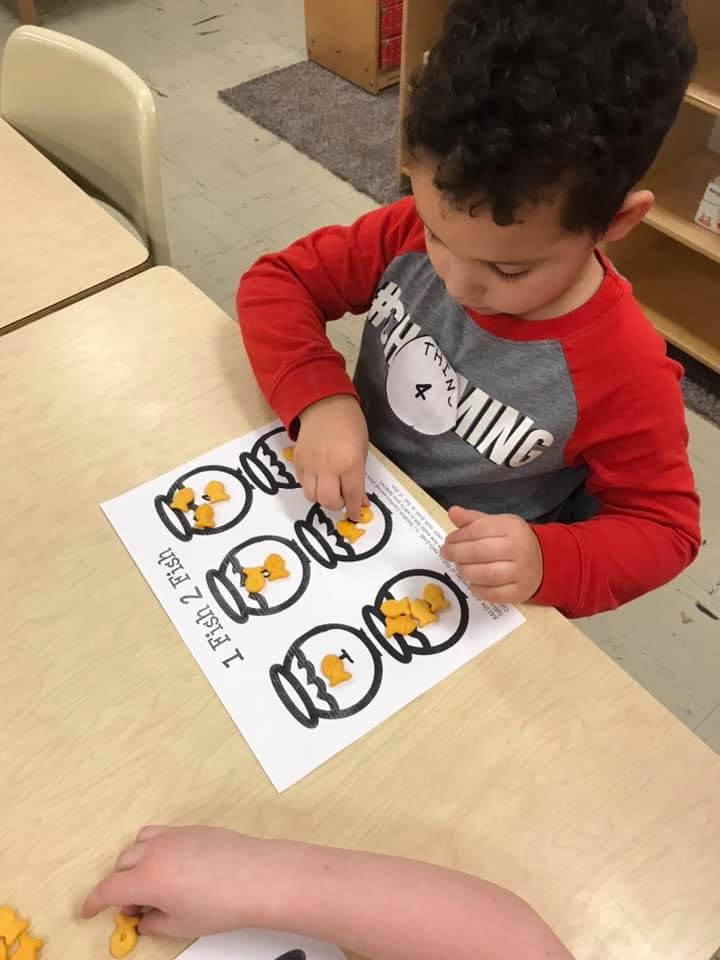 Child placing small yellow shapes into fishbowl outlines on a paper