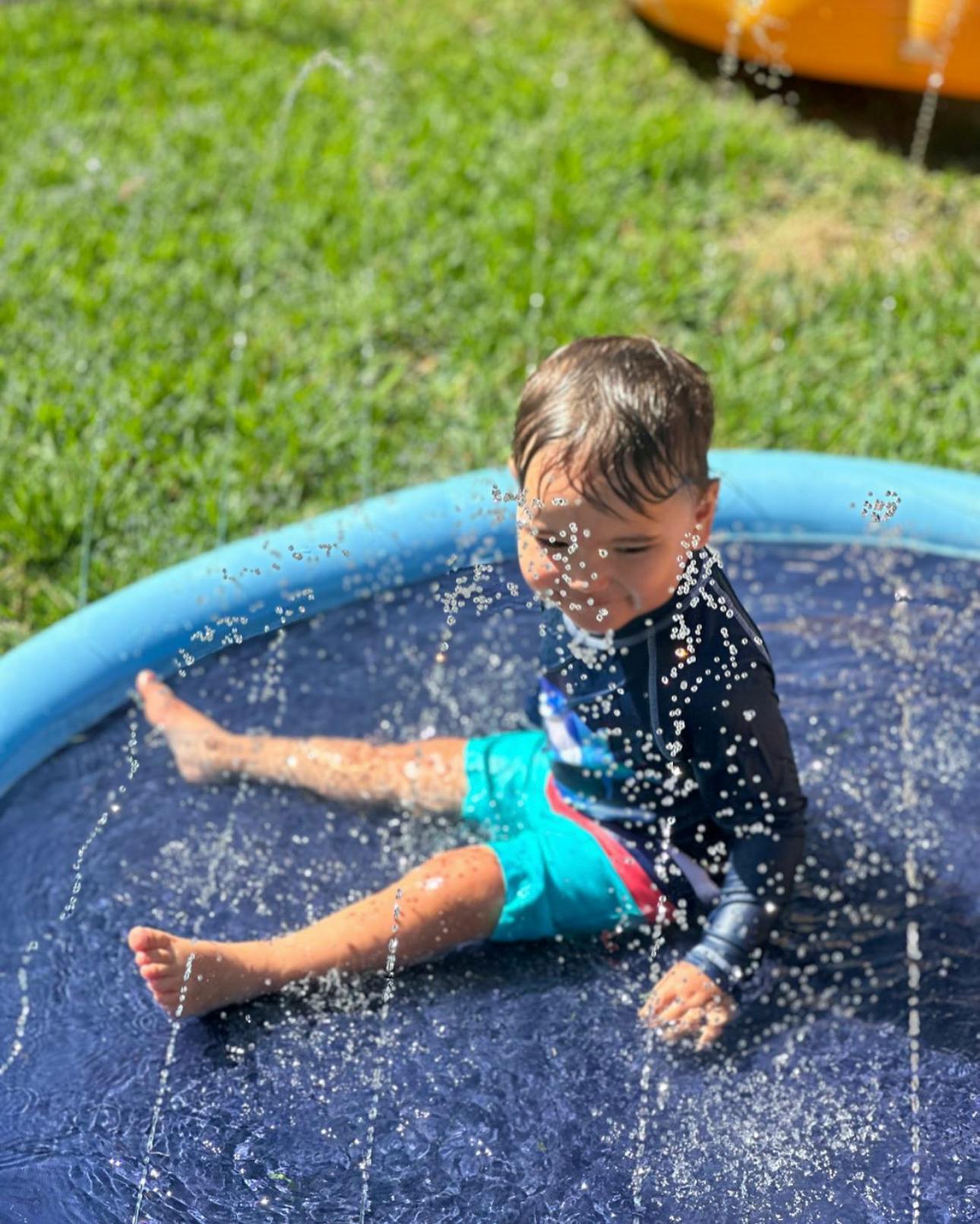 Child sitting in a blue inflatable pool with water spraying