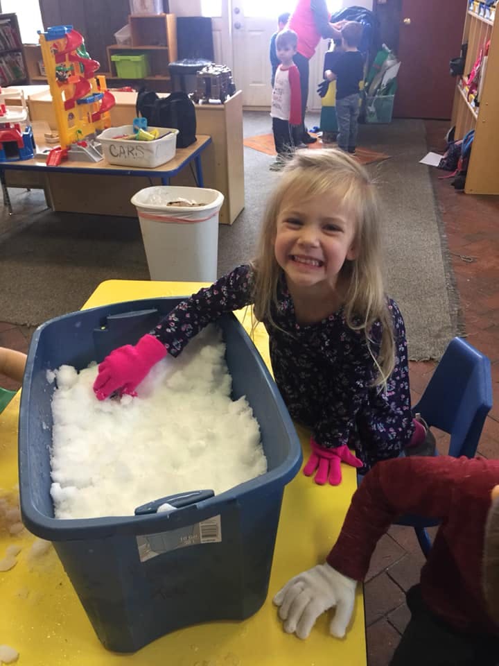 Child in pink gloves playing with snow in a bin