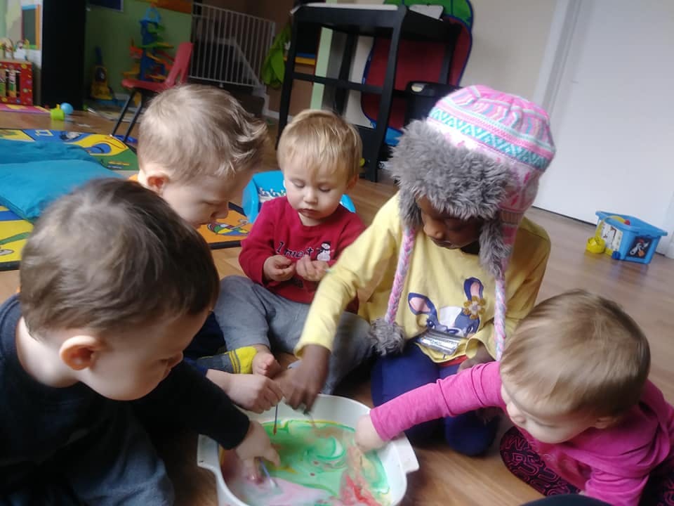 Four children playing with colorful liquid in a white container