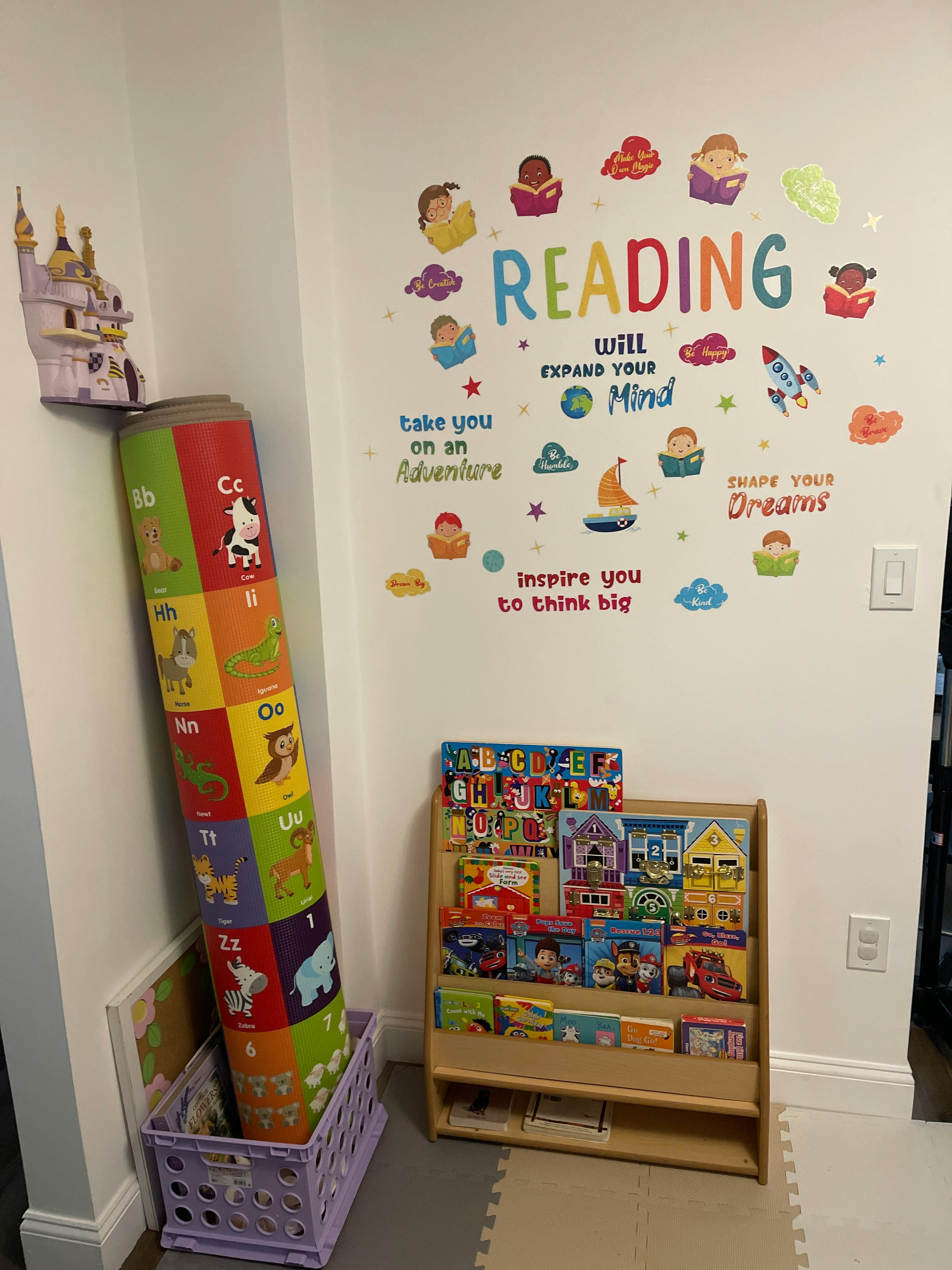 Reading-themed wall decals in a child's room with a bookcase and floor mat