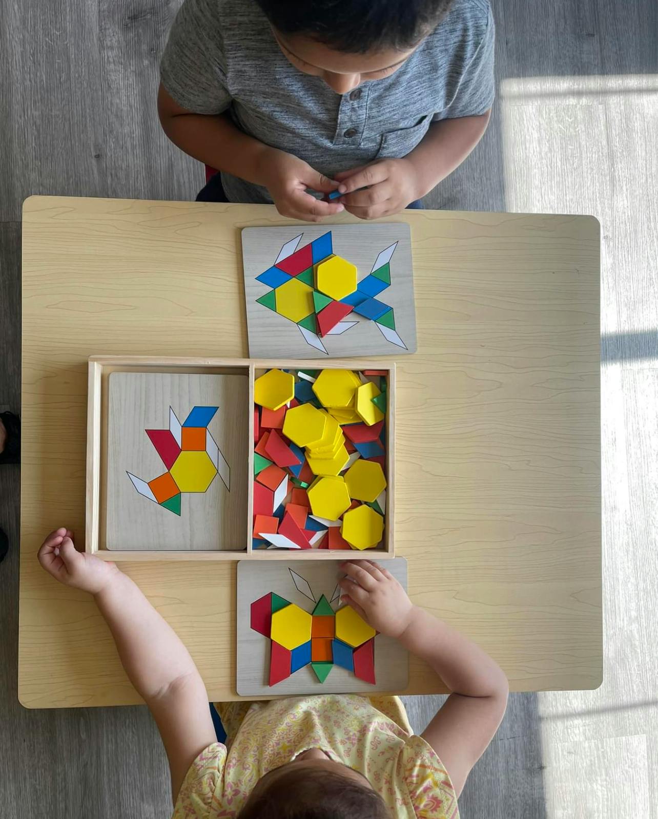 Two children playing with colorful geometric shape puzzles at a table