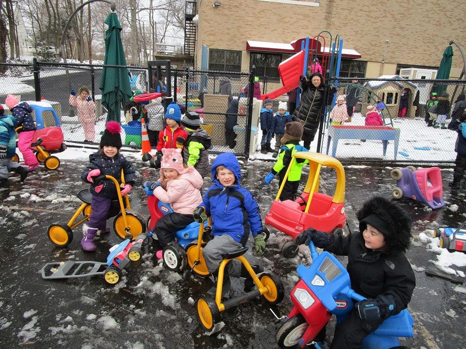 Children playing on tricycles and ride-on toys in a snowy playground