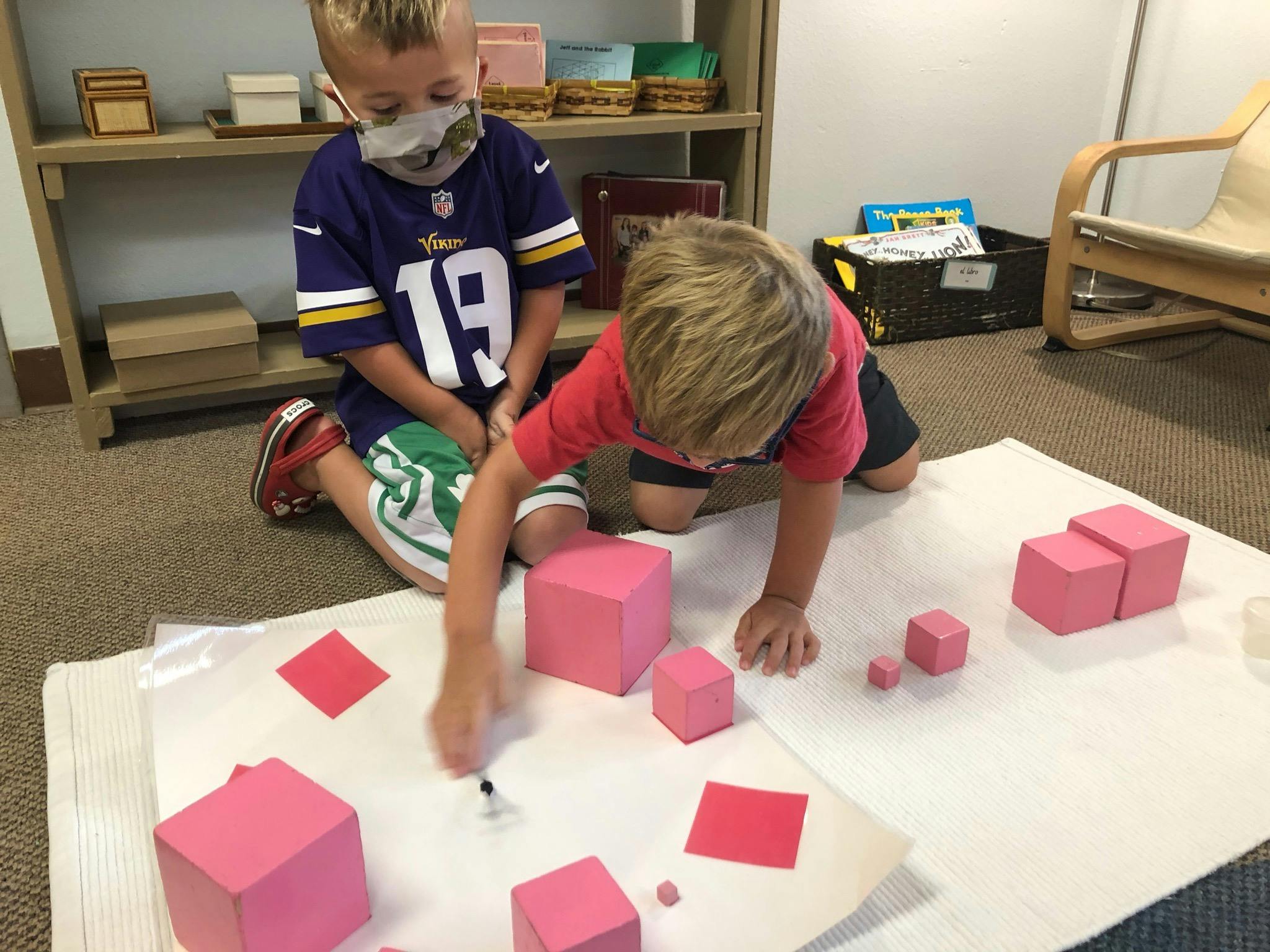 Two children playing with pink blocks and red squares on the floor