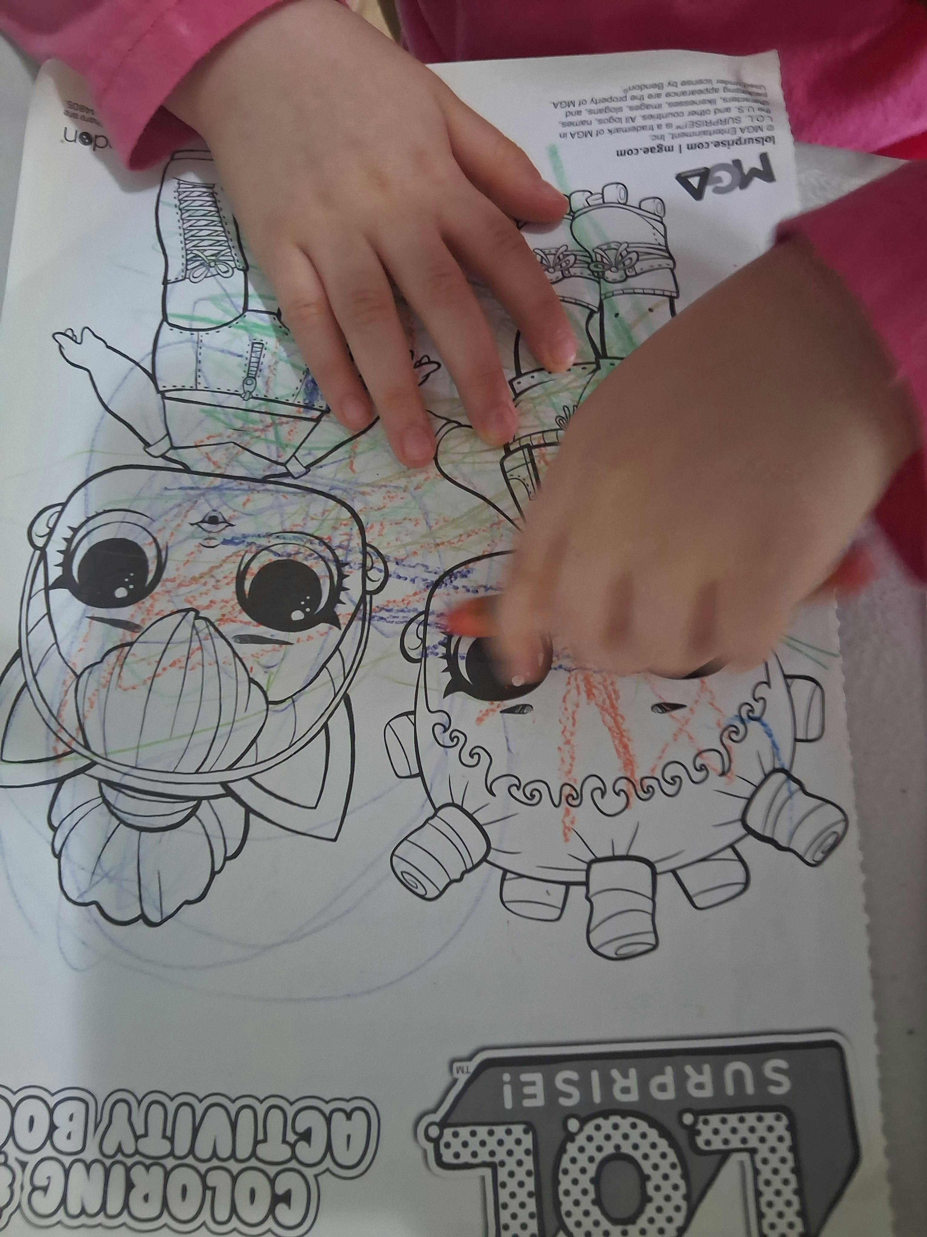 Child's hands coloring a coloring book with a picture of a cartoon doll