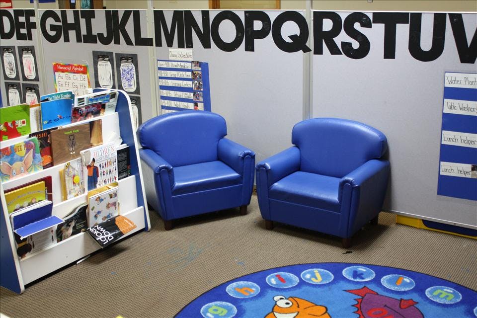 Children's reading nook with blue chairs, bookshelf, and alphabet on wall