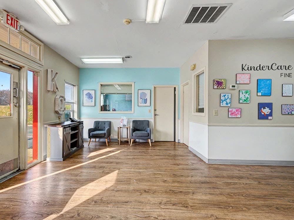 An empty waiting room with two chairs, wall art, and KinderCare Fine text on the wall