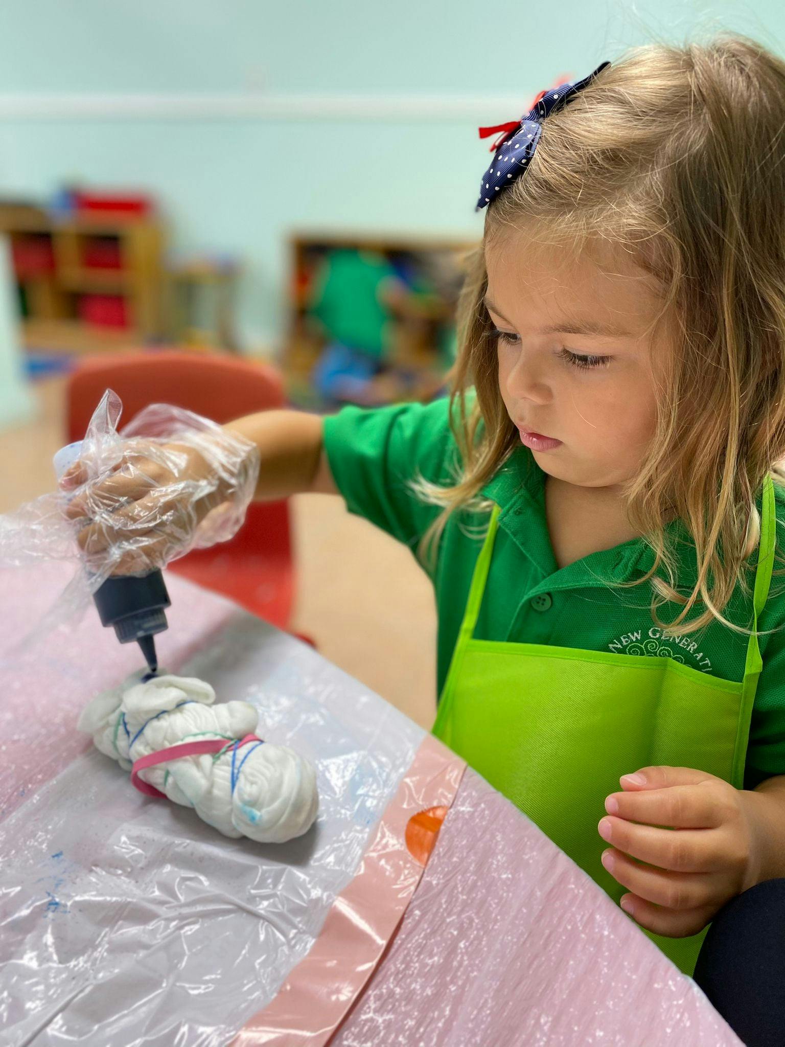 Child in an apron tie-dyeing a white fabric item with a squeeze bottle