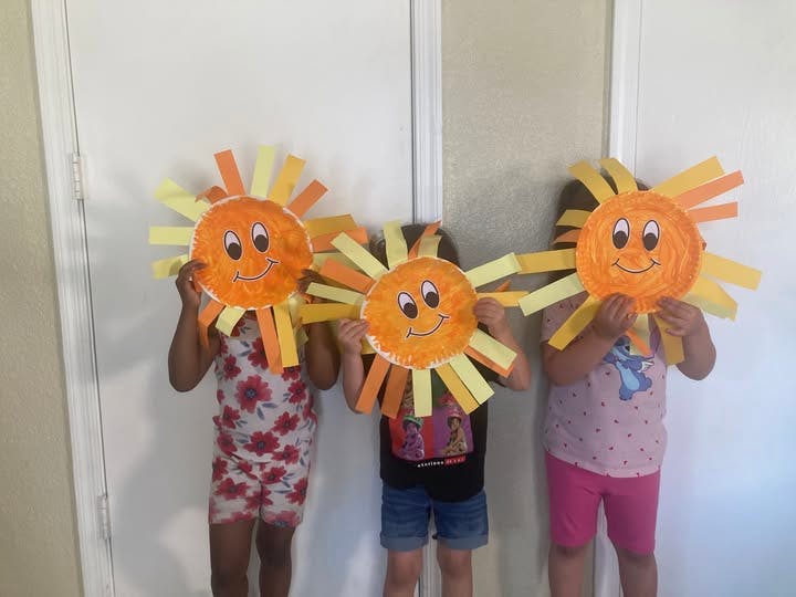 Three children holding paper sun crafts in front of their faces