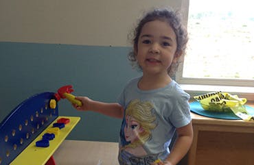 Child holding a toy hammer next to a toy workbench