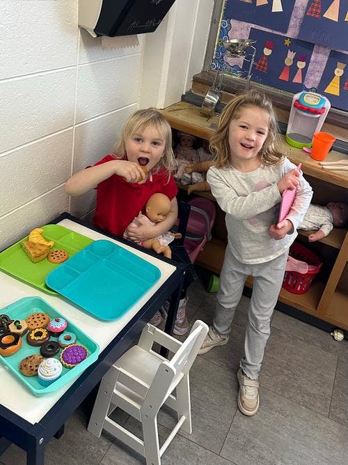 Two children playing with food trays and dolls in a classroom
