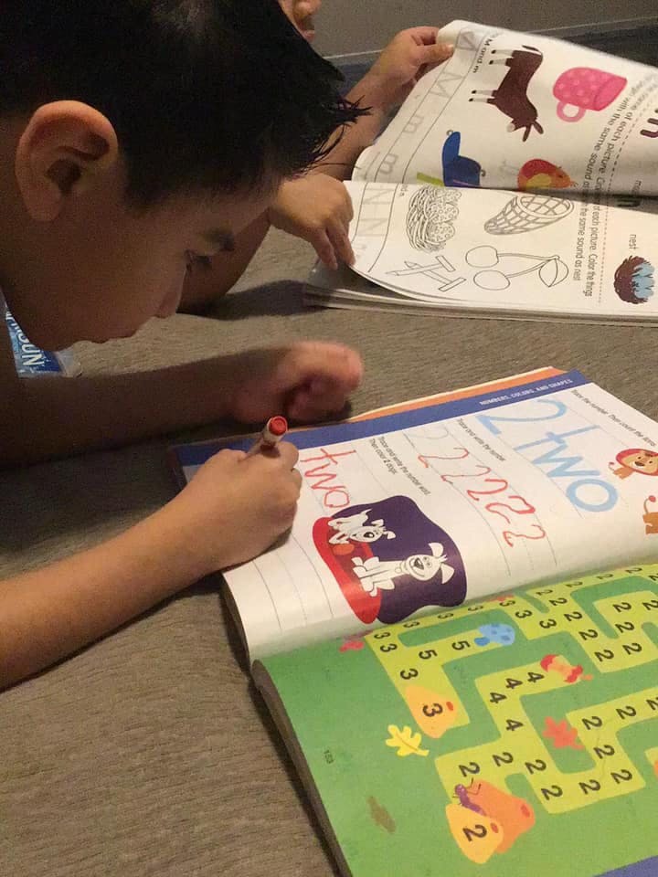 Child writing in a workbook with another child in the background