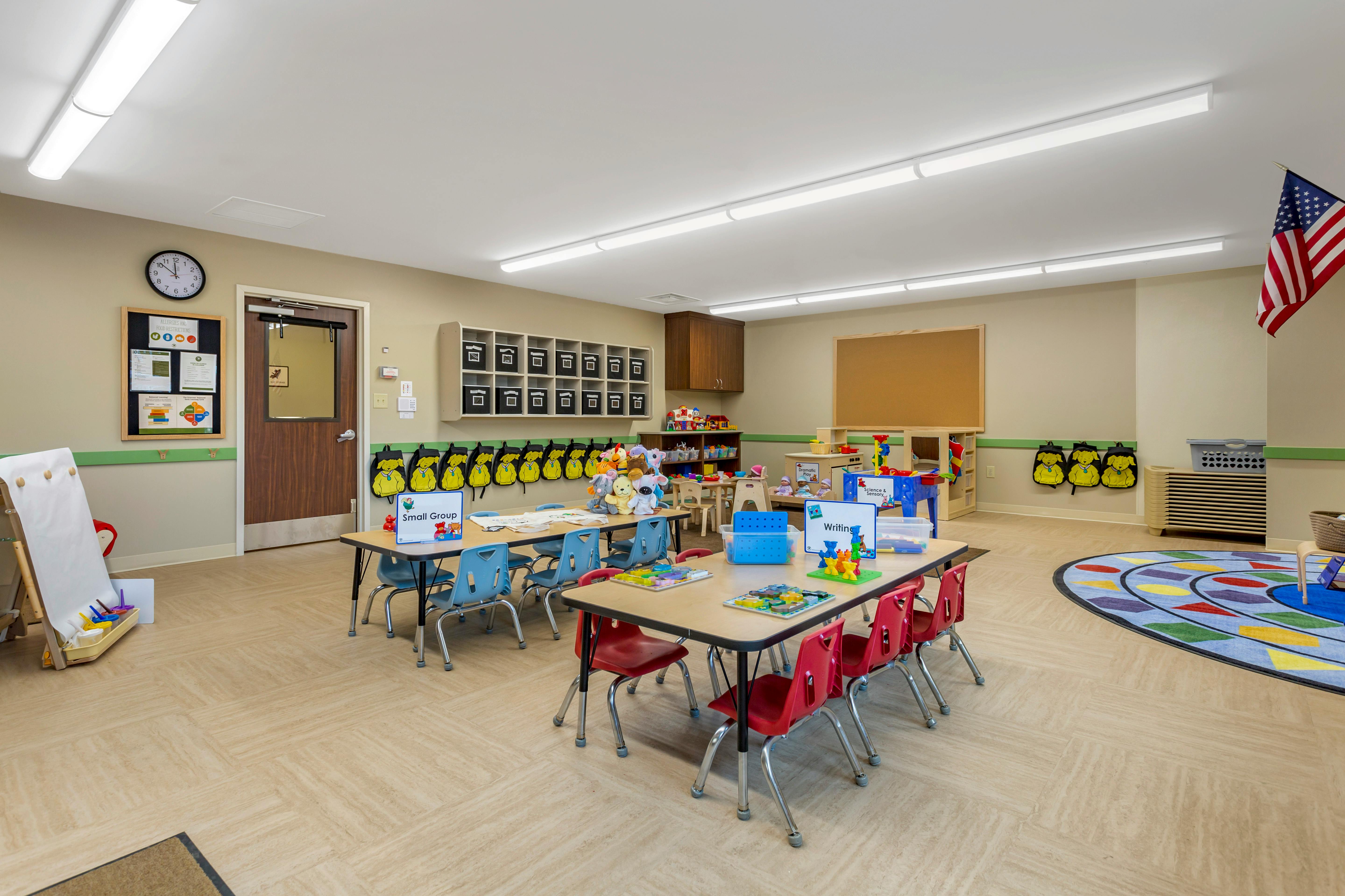 Classroom with small tables and chairs, shelves, play areas, and an American flag