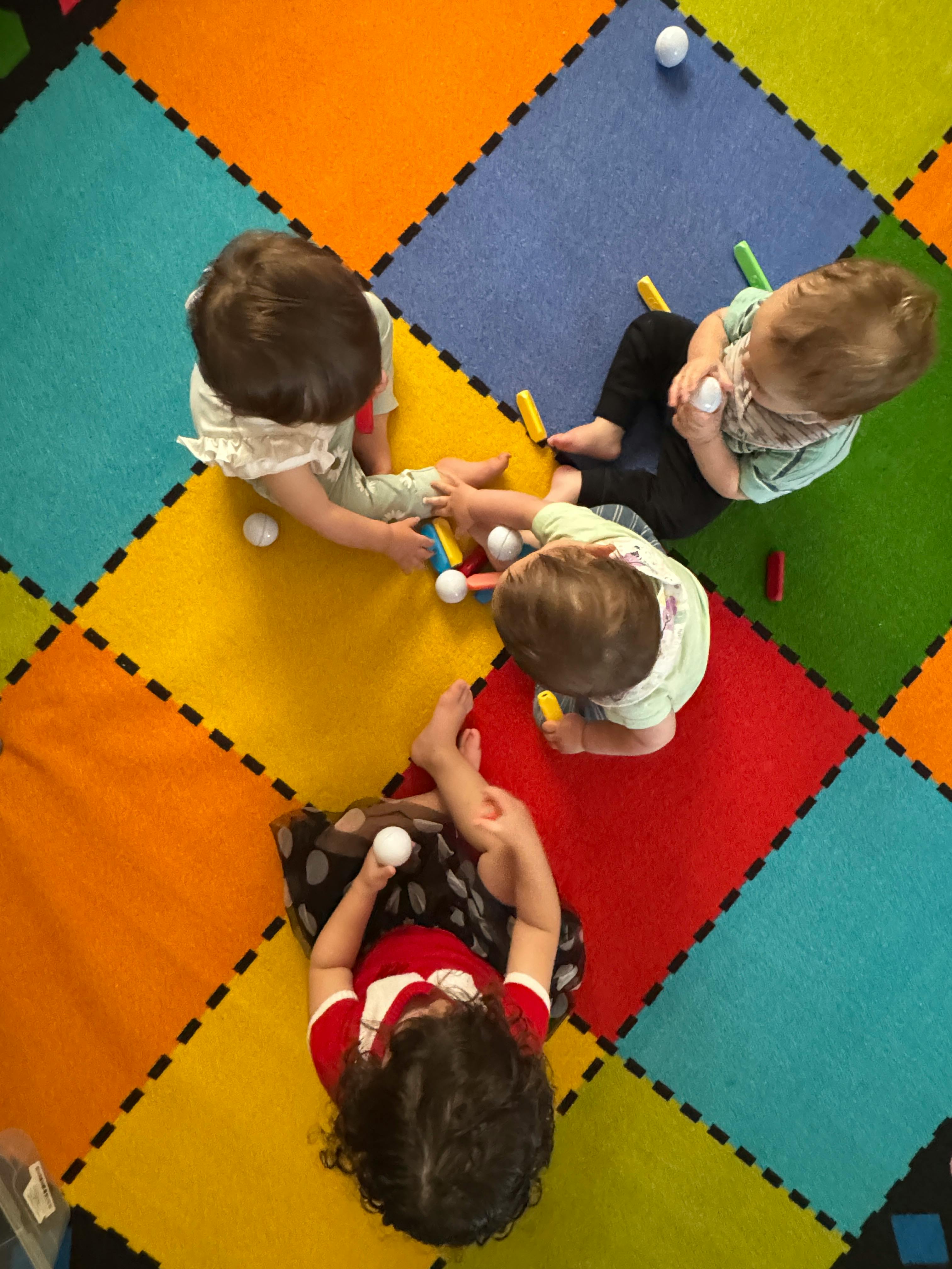 Three children playing with toys on a colorful mat