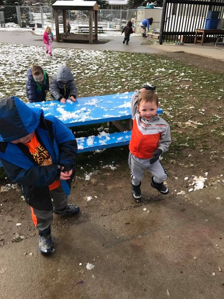 Children playing in a snowy outdoor area with a blue picnic table