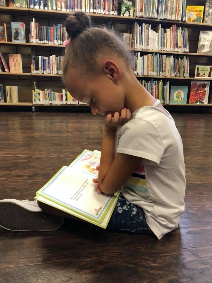 Child sitting on floor reading a book in a library