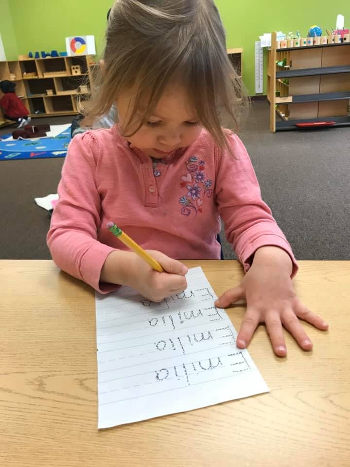 Child writing on paper with a pencil in a classroom