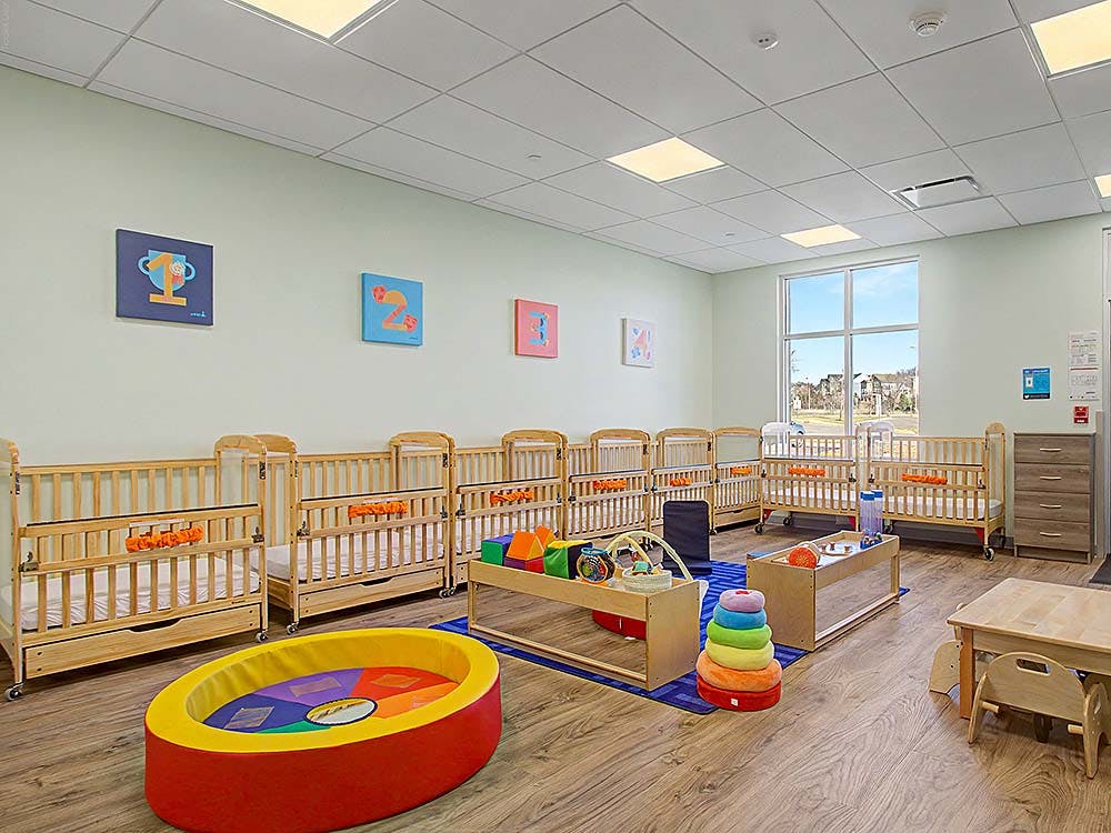 Classroom with wooden cribs, play mats, and a small table with chairs