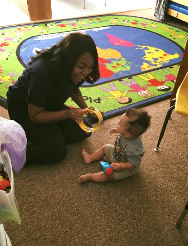 Person kneeling and holding a tambourine for a child sitting on the floor