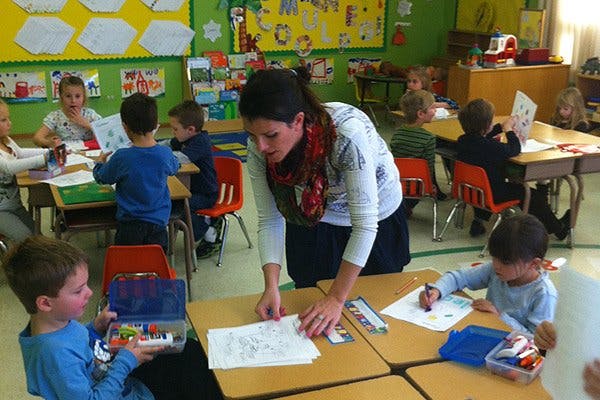 Adult person helping children with schoolwork in a classroom