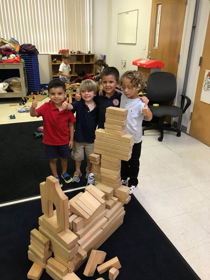 Four children standing with a large structure made of wooden blocks