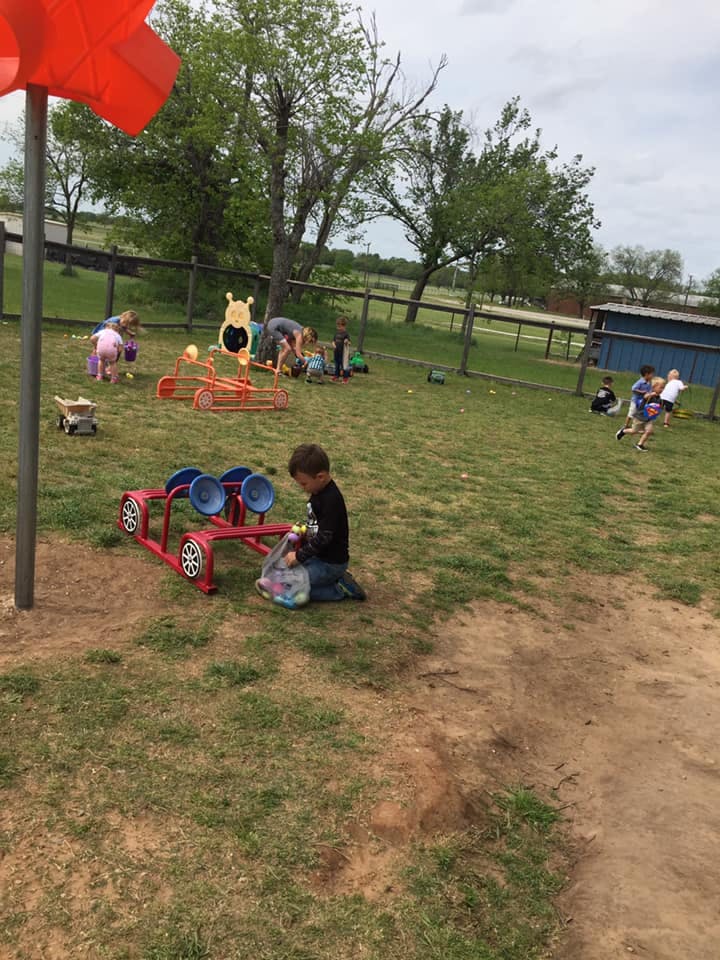 Child kneeling on grass next to a red toy car, holding a bag