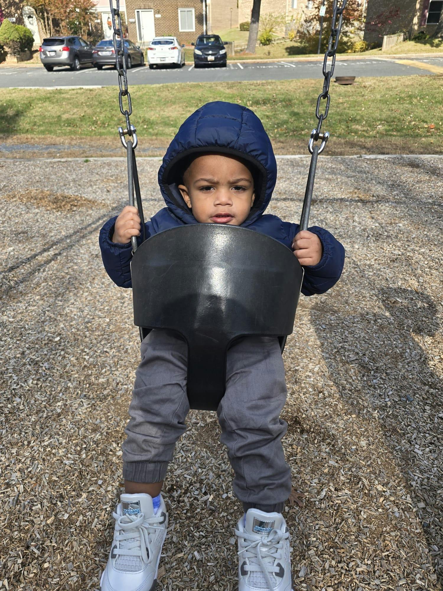 Child in a blue coat sitting in a swing at a playground