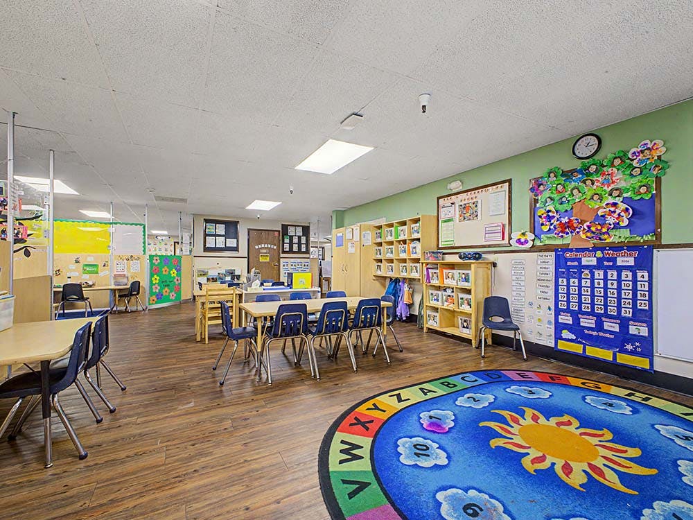 An empty classroom with small tables and chairs, and a colorful rug on the floor