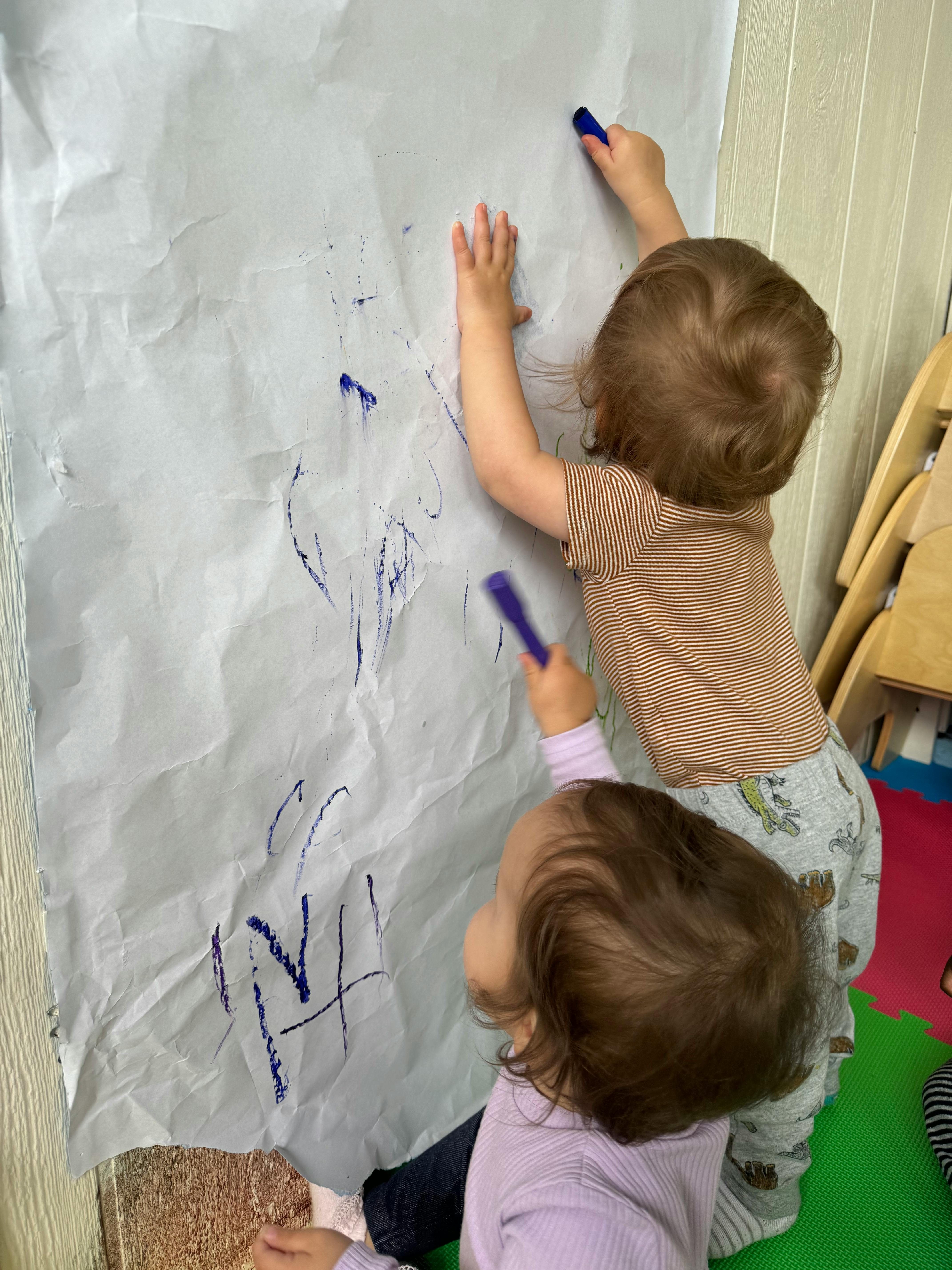 Two children drawing on a large sheet of paper with markers